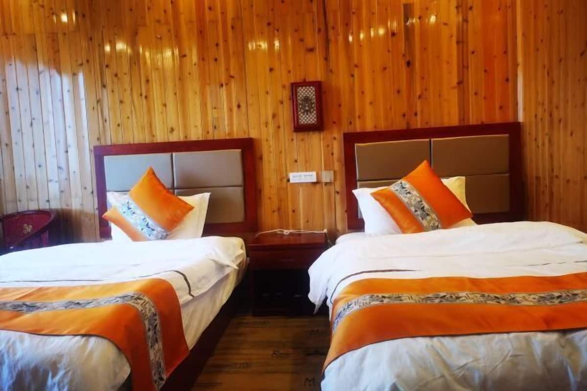 A room with two beds, wooden walls, a small table, and a wall-mounted light fixture.