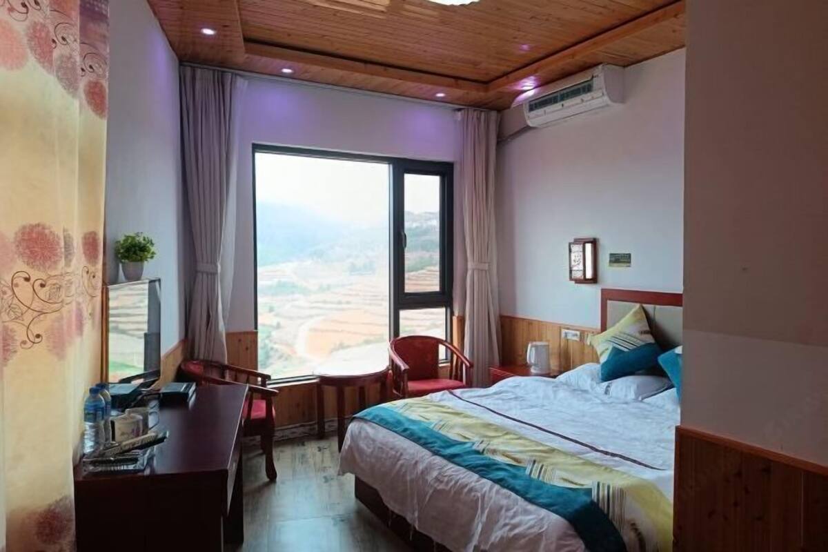 A hotel room with a large bed, a desk, a chair, and a window with a view of the countryside.