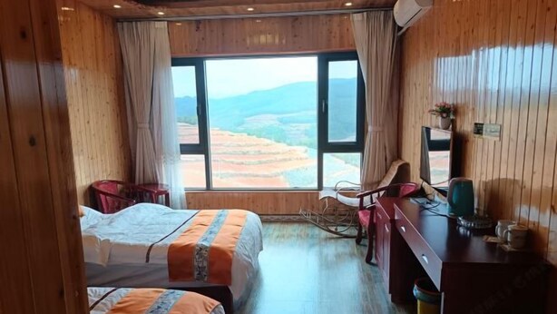 Une chambre avec deux lits, un bureau, une chaise et une vue sur des champs en terrasses.