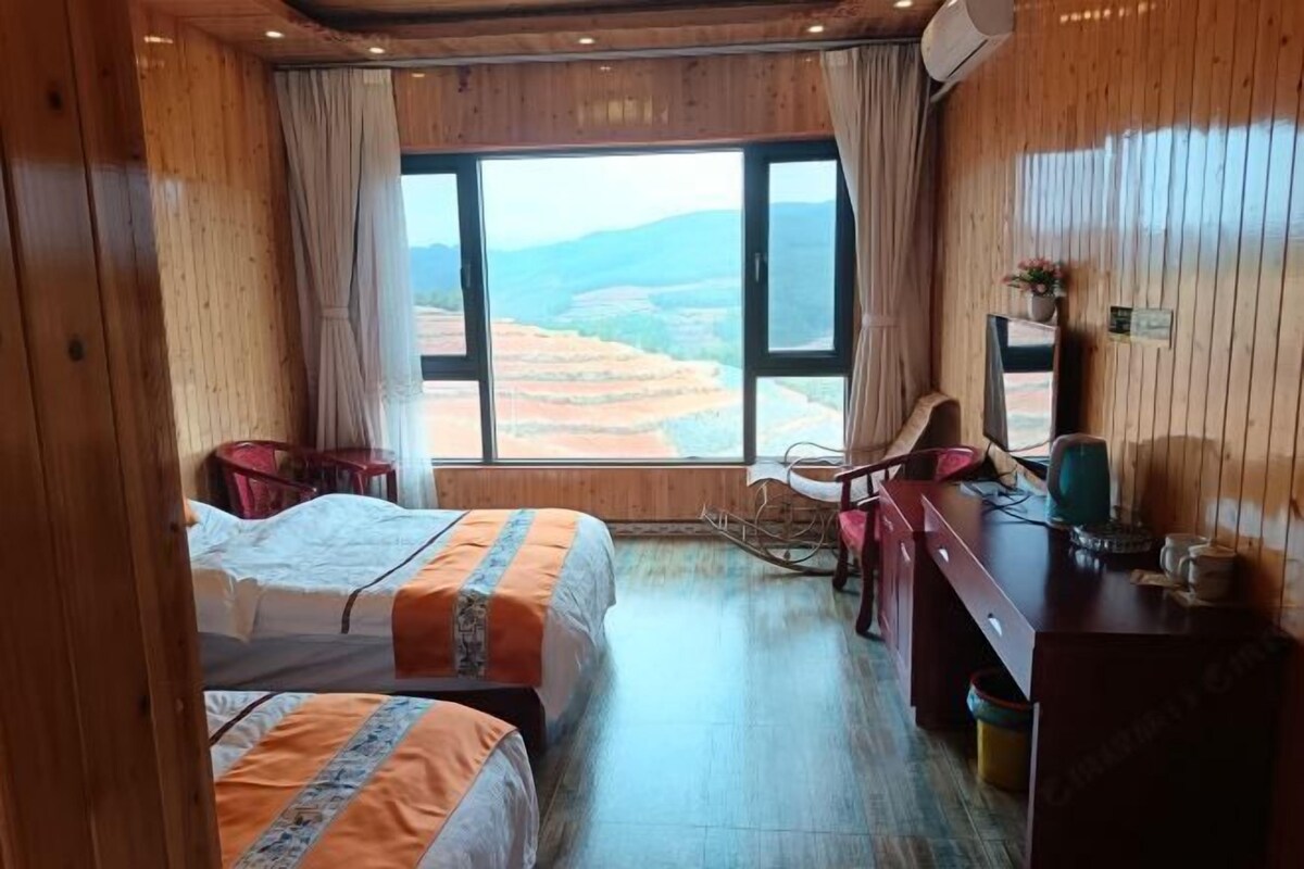 A room with two beds, a desk, a chair, and a view of terraced fields.