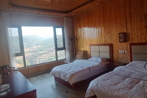 A room with two beds, a wooden ceiling, a large window with a view of a valley, and a small table with a kettle. - Hongtu Qicai Renjia Hostel (Kunming)