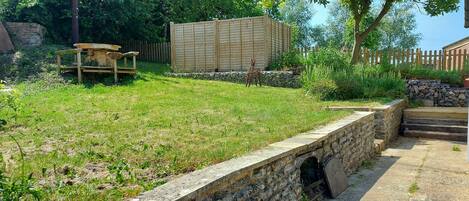 A stone retaining wall with a small opening, a wooden deck, and a wooden fence in a garden setting.