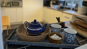 A kitchen with a blue and white tiled backsplash, a blue teapot on a tray, two patterned cups, and a bowl of sugar cubes.