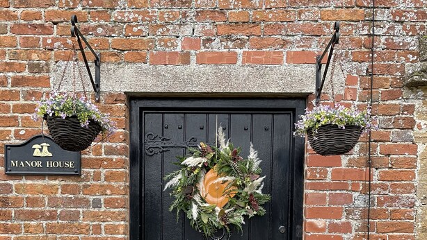 A black door with a wreath, a sign reading "MANOR HOUSE", and a stone cat statue on the left.