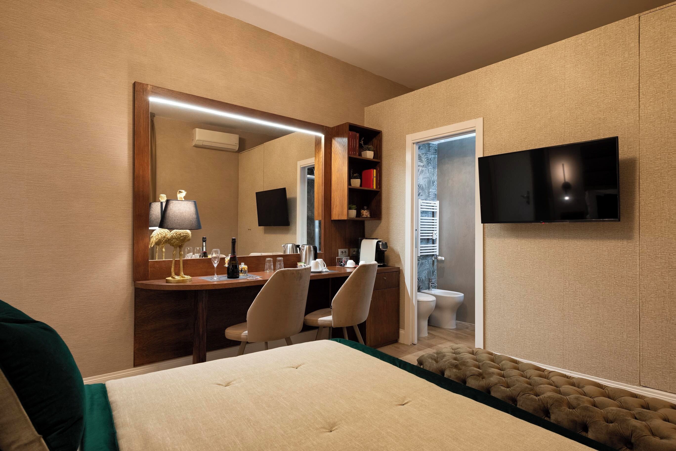 Ein Hotelzimmer mit einem Bett, einem Schreibtisch mit Stühlen, einem Fernseher, einem Spiegel und einem Kleiderschrank.