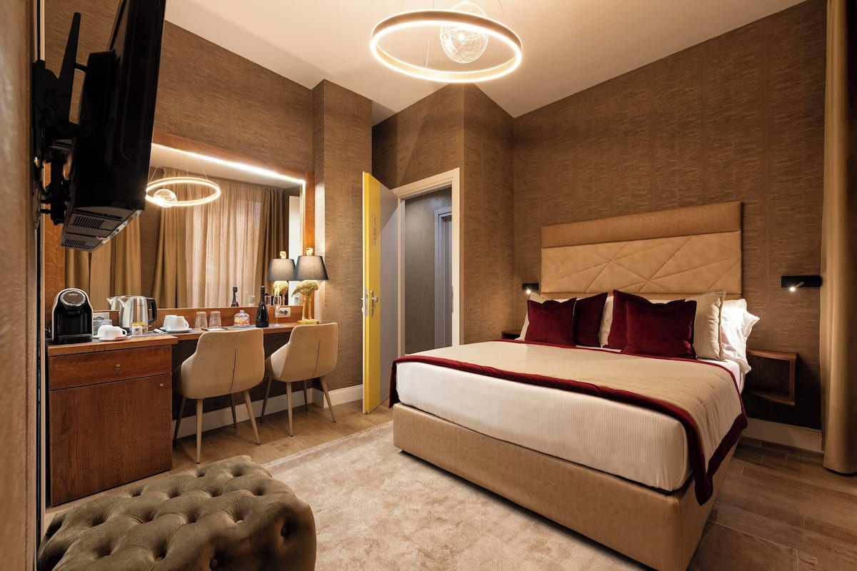 Moderni hotellihuone, jossa on suuri sänky, työpöytä tuolilla, peilillä varustettu meikkipöytä ja riippuvalaisin.