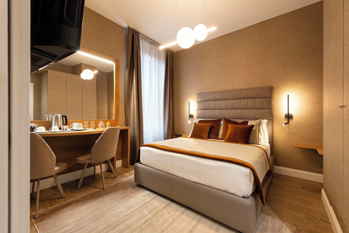 Hotellihuone, jossa on suuri sänky, työpöytä tuolilla, peili ja televisio.