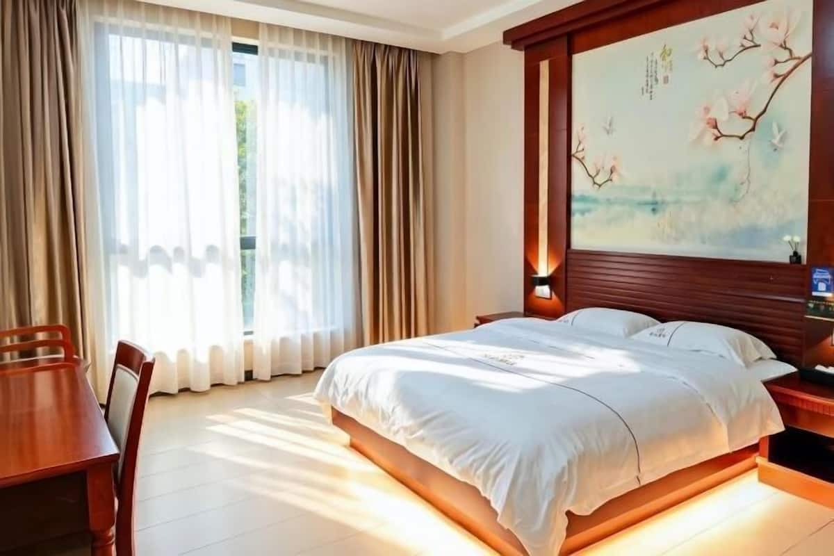 Una habitación de hotel con una cama, una mesita de noche de madera, una mesa y un cuadro en la pared.