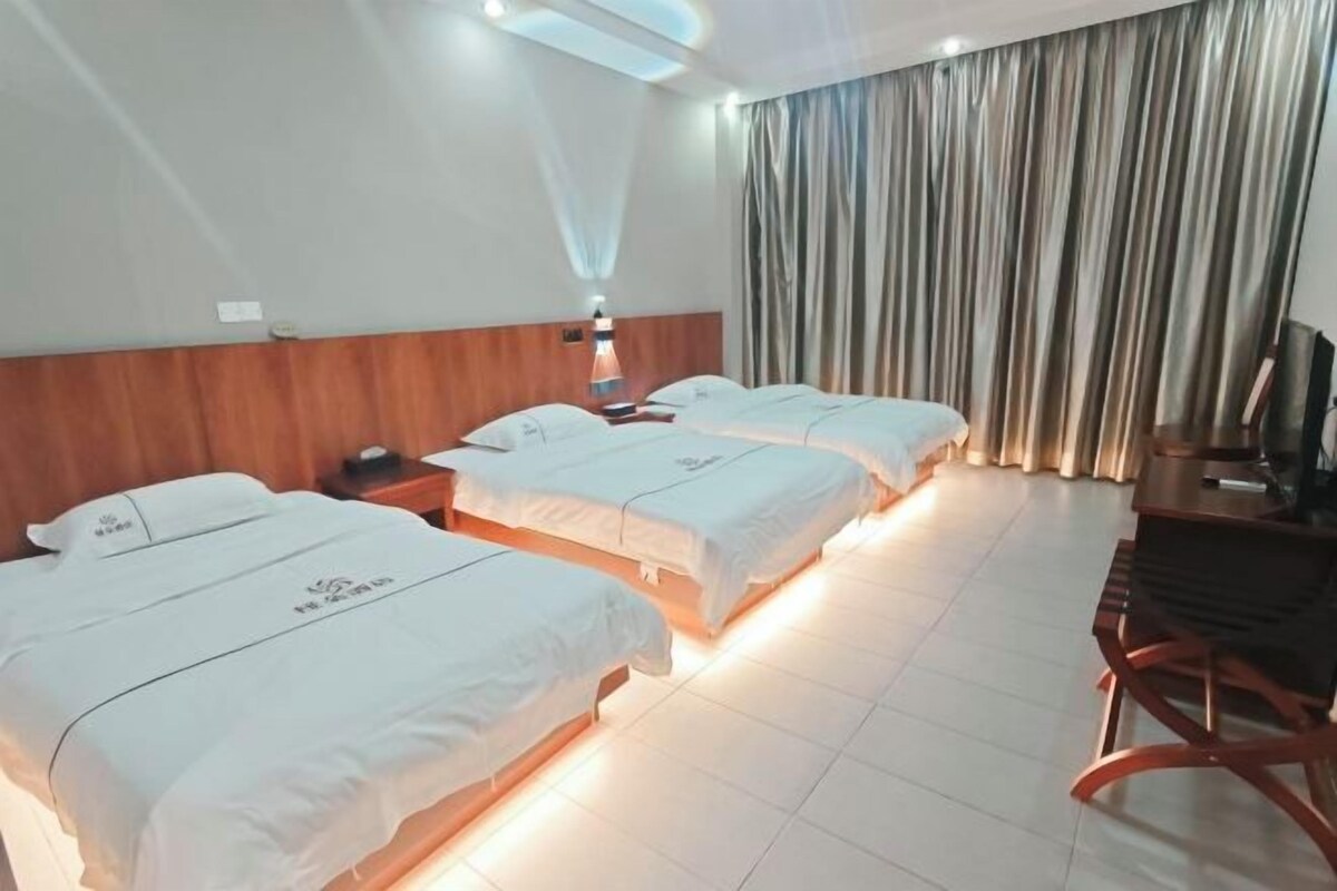 Habitación de hotel con tres camas, cabecera de madera, escritorio con silla y televisor.