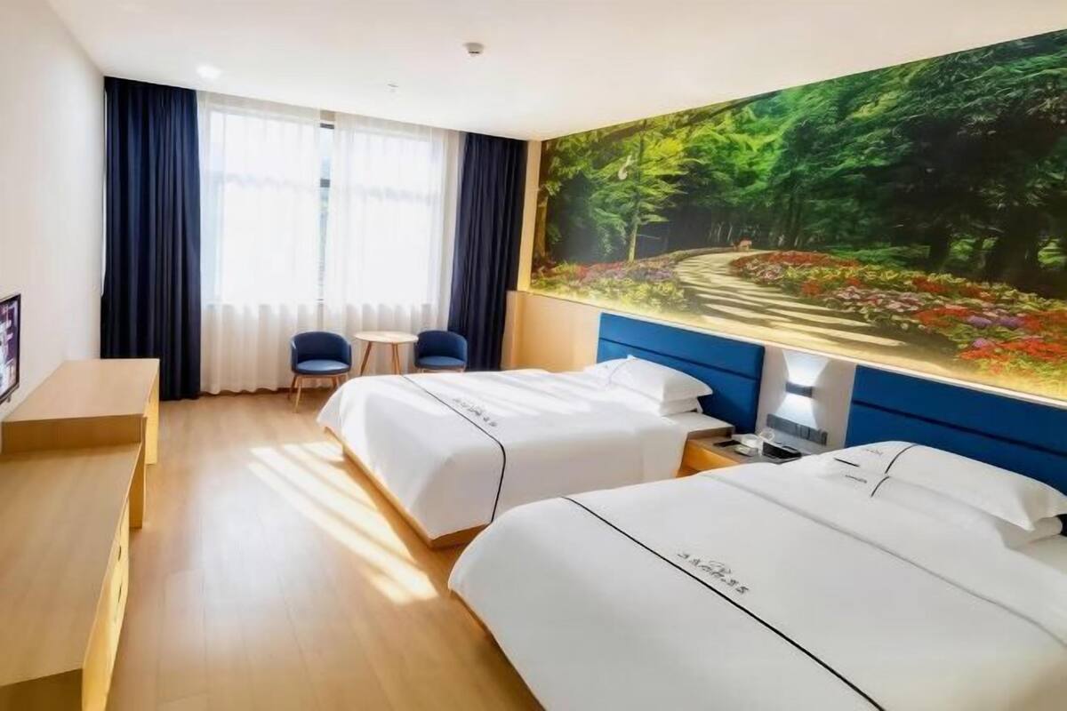 Habitación de hotel con dos camas, un escritorio, una silla, un televisor y un cuadro grande con un paisaje boscoso.