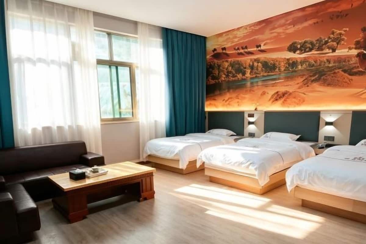 Habitación de hotel con dos camas, un sofá, una mesa de centro de madera y un cuadro grande con un paisaje en la pared.
