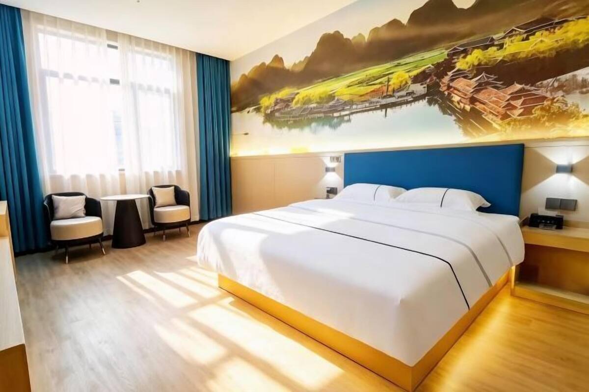 Habitación de hotel con una cama grande, un escritorio, dos sillas y un mural de un paisaje.