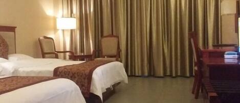A hotel room with two beds, a desk, a chair, and a lamp.