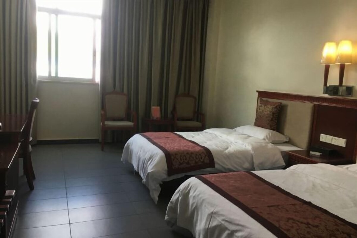 A hotel room with two beds, a desk, chairs, and a window with curtains.