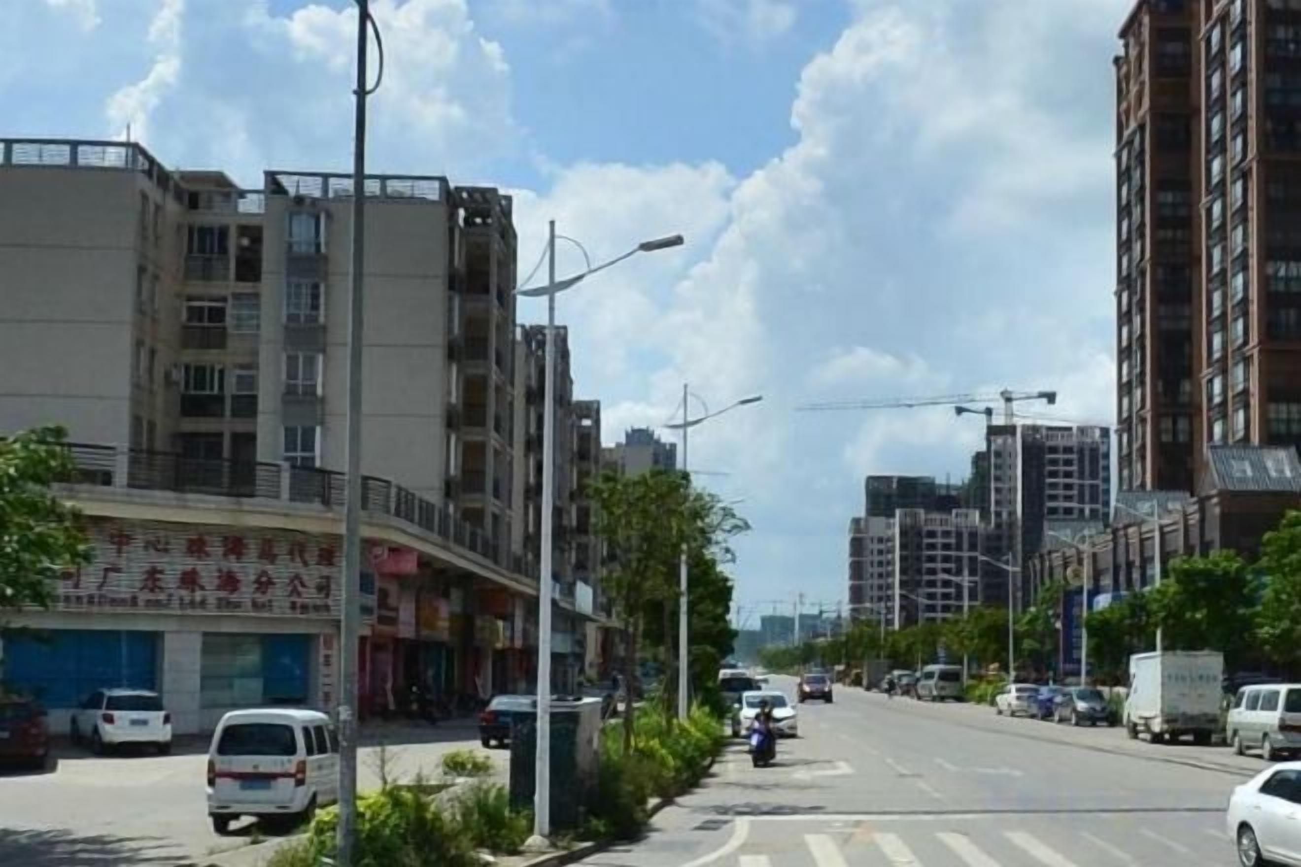 A multi-story building with commercial establishments on the ground floor, a clear sky, and a road with vehicles.