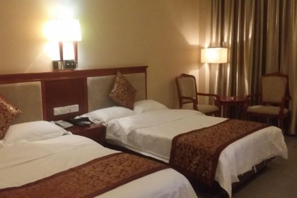 A hotel room with two beds, a nightstand, a chair, and a lamp.