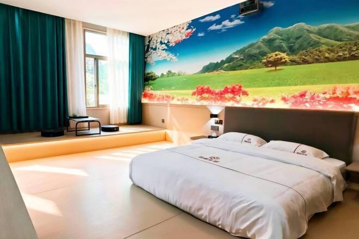 Un dormitorio con una cama grande, una ventana con cortinas, una lámpara de pared y un mural de un paisaje.