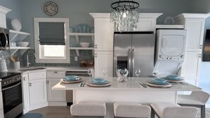 Una cucina moderna con mobili bianchi, un'isola centrale con sgabelli da bar, un frigorifero in acciaio inossidabile e un lampadario.