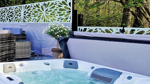 Un bain à remous rempli d’eau, entouré de meubles en osier et d’une clôture blanche décorative.