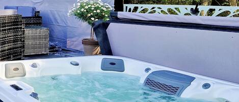 Un jacuzzi con agua, rodeado de mobiliario de mimbre y una cerca blanca decorativa.