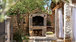 A stone-built outdoor fireplace with logs, surrounded by greenery and a stone wall. - Typical Istrian stone house with garden, pool and sauna, Pets are welcome. (Sveti Lovrec)
