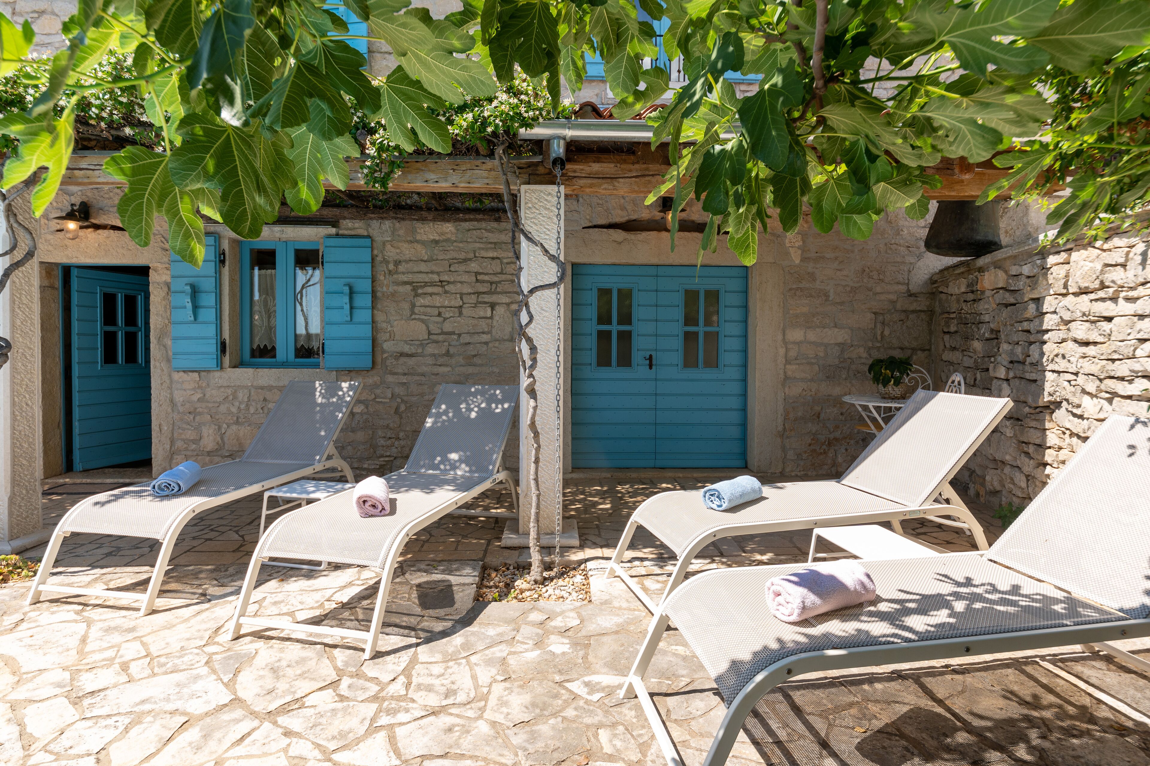Une terrasse en pierre avec quatre chaises longues, chacune agrémentée d’une serviette.