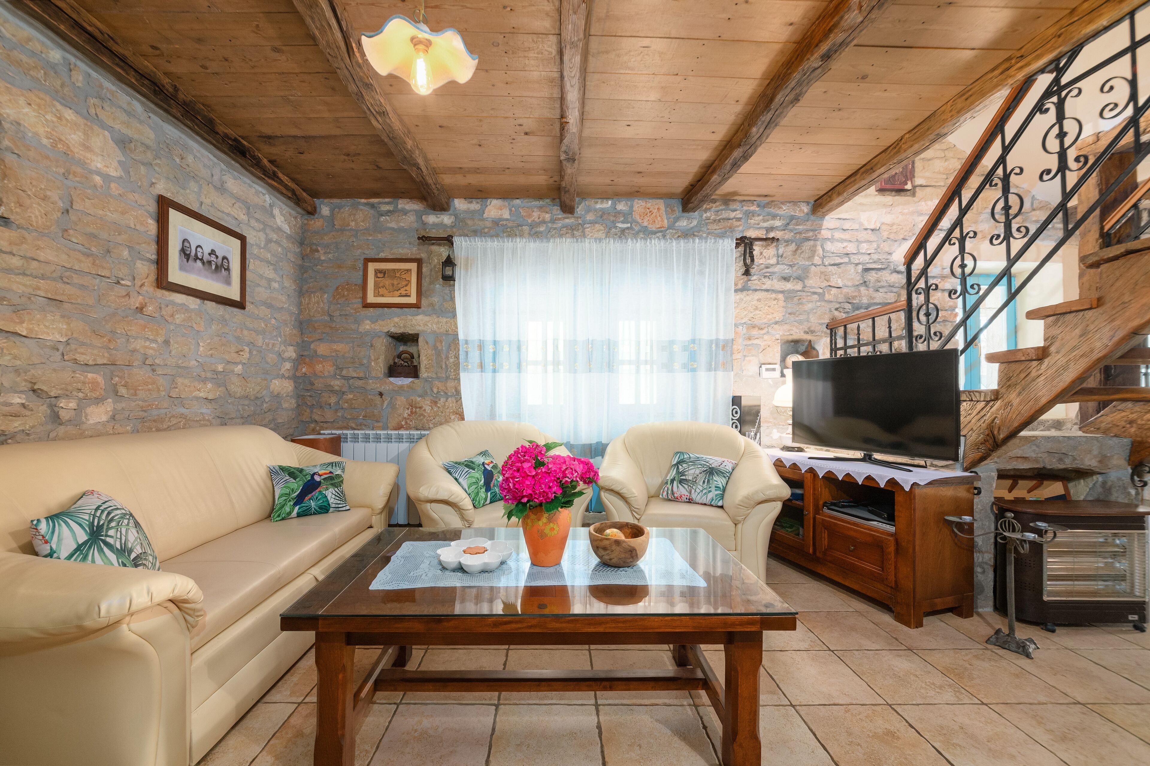 Ein gemütliches Wohnzimmer mit Steinwand, Holzbalkendecke, einer Couch, einem Couchtisch mit Dekoration, einem Fernseher und einem Kamin.