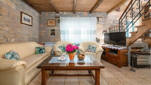 A cozy living room with a stone wall, wooden ceiling beams, a sofa, a coffee table with decorative items, a television, and a fireplace. - Typical Istrian stone house with garden, pool and sauna, Pets are welcome. (Sveti Lovrec)
