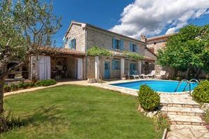 Una villa de piedra con piscina, porche cubierto y jardín bien cuidado.