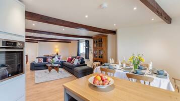 A modern kitchen with built-in appliances, a dining area with a wooden table set for a meal, and a cozy living room with a sofa and a lamp.