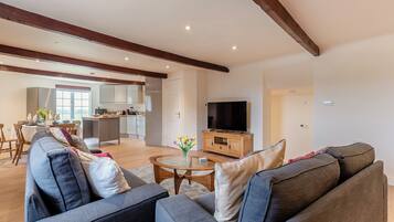 A modern living room with a grey sofa, a wooden TV stand, and a dining area with a table and chairs.