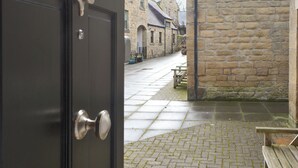 A stone building with a paved courtyard, a wooden bench, and a door with a metal handle. - 1 bedroom accommodation in Alnwick (Alnwick)