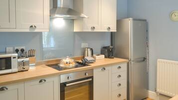 A modern kitchen with white cabinets, a stainless steel range hood, a built-in oven, a microwave, a refrigerator, and a coffee maker.