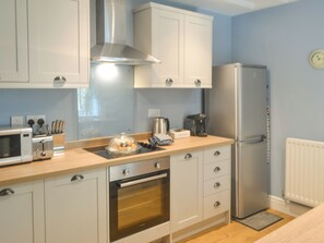 Una cocina moderna con gabinetes blancos, una campana extractora de acero inoxidable, horno integrado, microondas, refrigerador y cafetera.