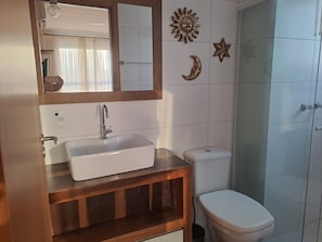 Ein Badezimmer mit weißem Waschbecken, einer Holzwaschkommode, einer Toilette und einer Duschkabine aus Glas.
