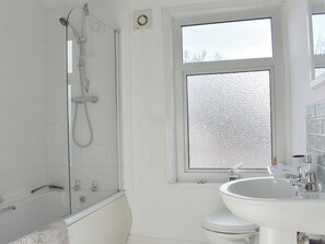 A bathroom with a glass-enclosed shower, a white sink, and a window with frosted glass.