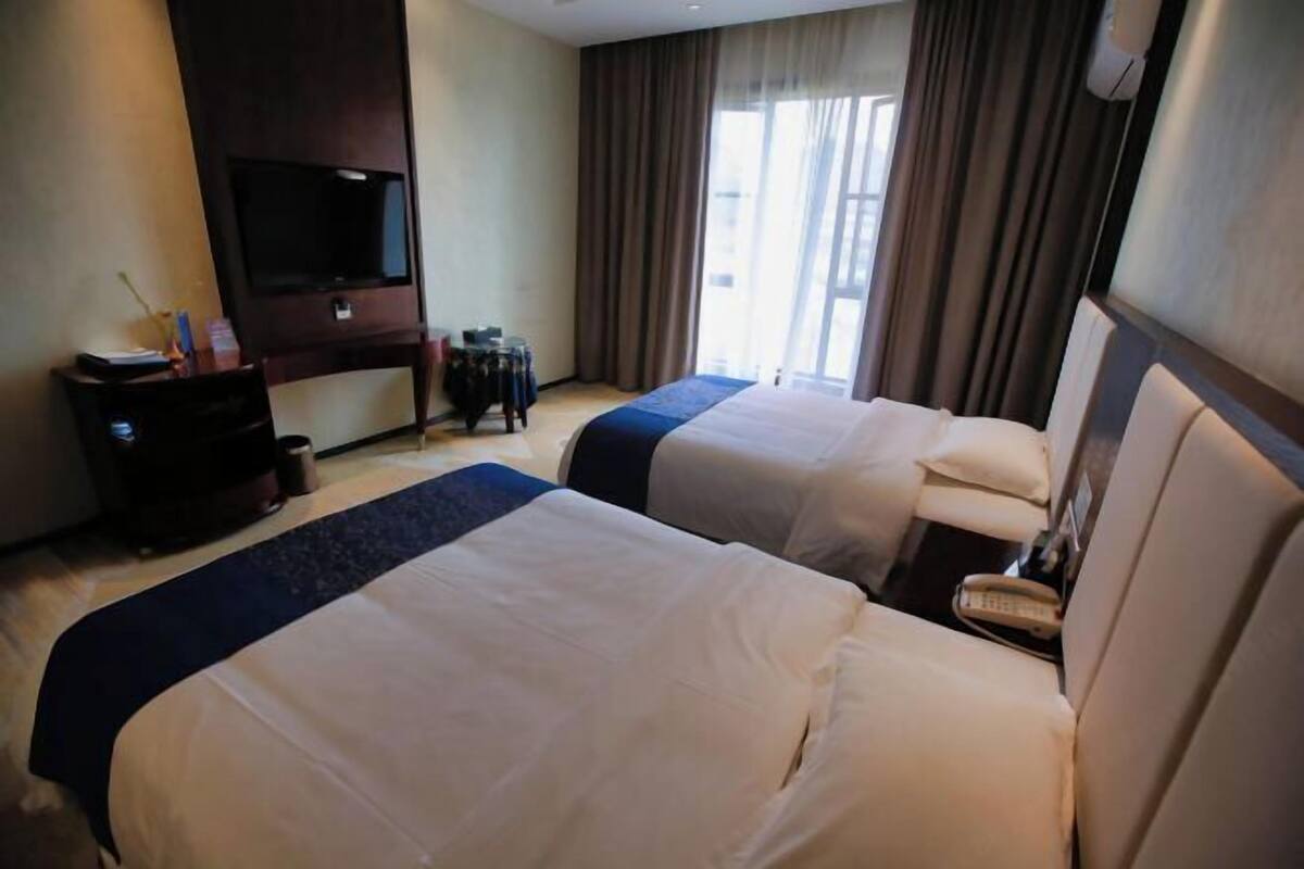 A hotel room with two beds, a TV, and a window with curtains.
