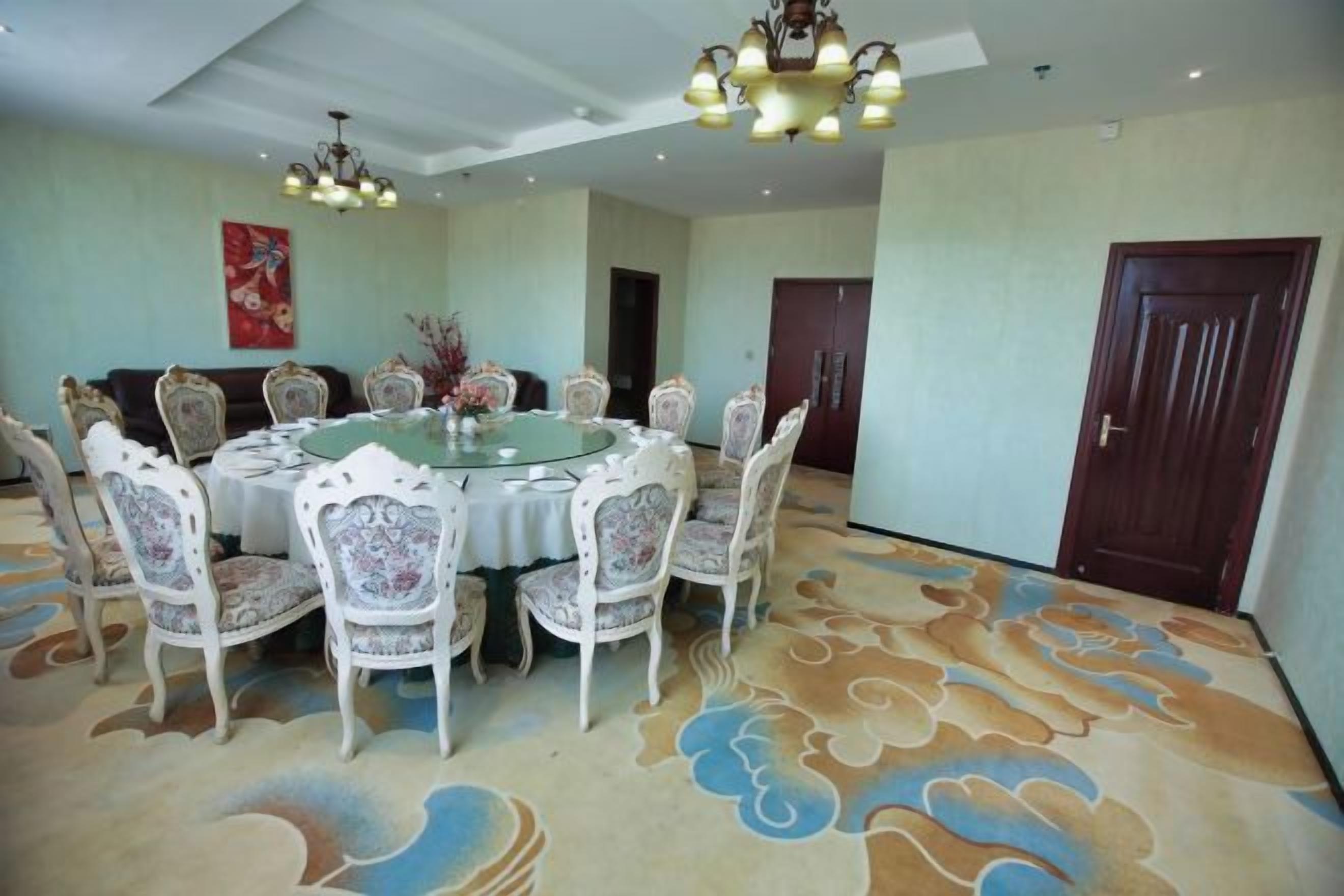 A dining area with a round table surrounded by chairs, a patterned carpet, and a chandelier.