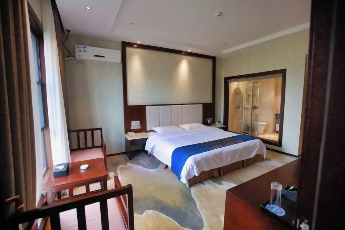 A hotel room with a bed, a desk, a chair, a large mirror, and a window.