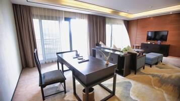 A modern hotel room with a dining table, a sofa, a TV, and a large window with curtains.
