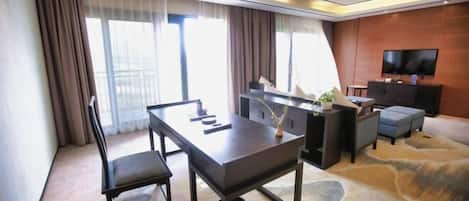 Una habitación de hotel moderna con una mesa de comedor, un sofá, un televisor y un ventanal con cortinas.