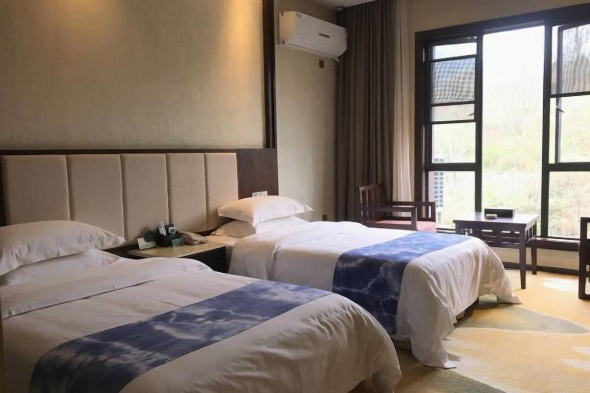 A hotel room with two beds, a window with curtains, a small table, and a chair.