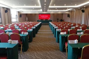 A conference room with rows of tables and chairs, a podium, and a presentation screen. - Guifeng Hotel Zhenfeng (Zhenfeng)