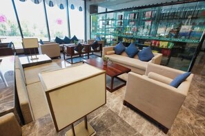Um saguão de hotel com disposição de assentos, uma mesa de centro e uma vitrine de vidro com objetos.