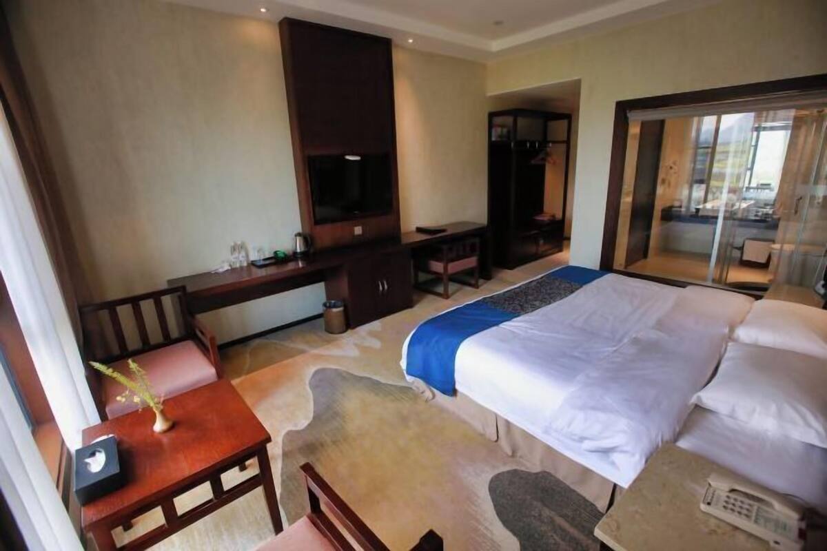 A hotel room with a bed, a desk, a TV, a wardrobe, and a view of the outside.