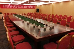 Un salón de conferencias con una larga mesa, sillas rojas y piso alfombrado.