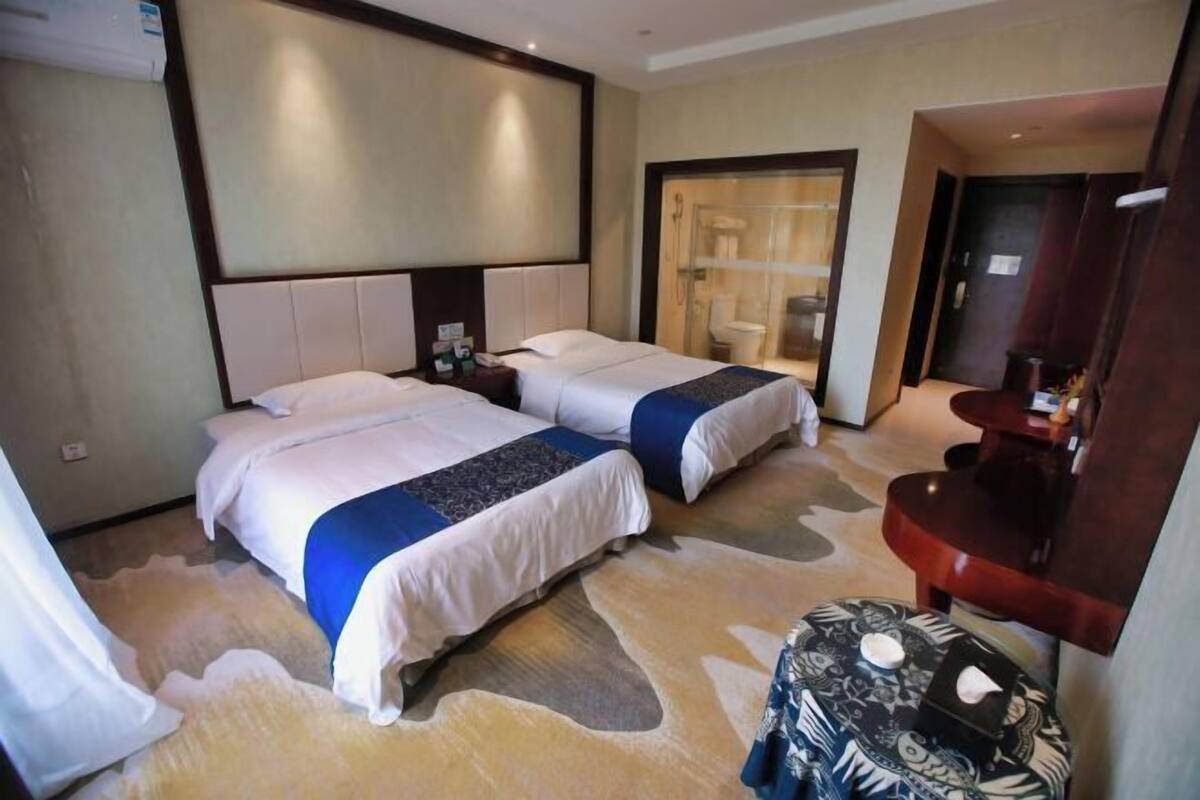 A hotel room with two beds, a small round table, a mirror, and a shower area.