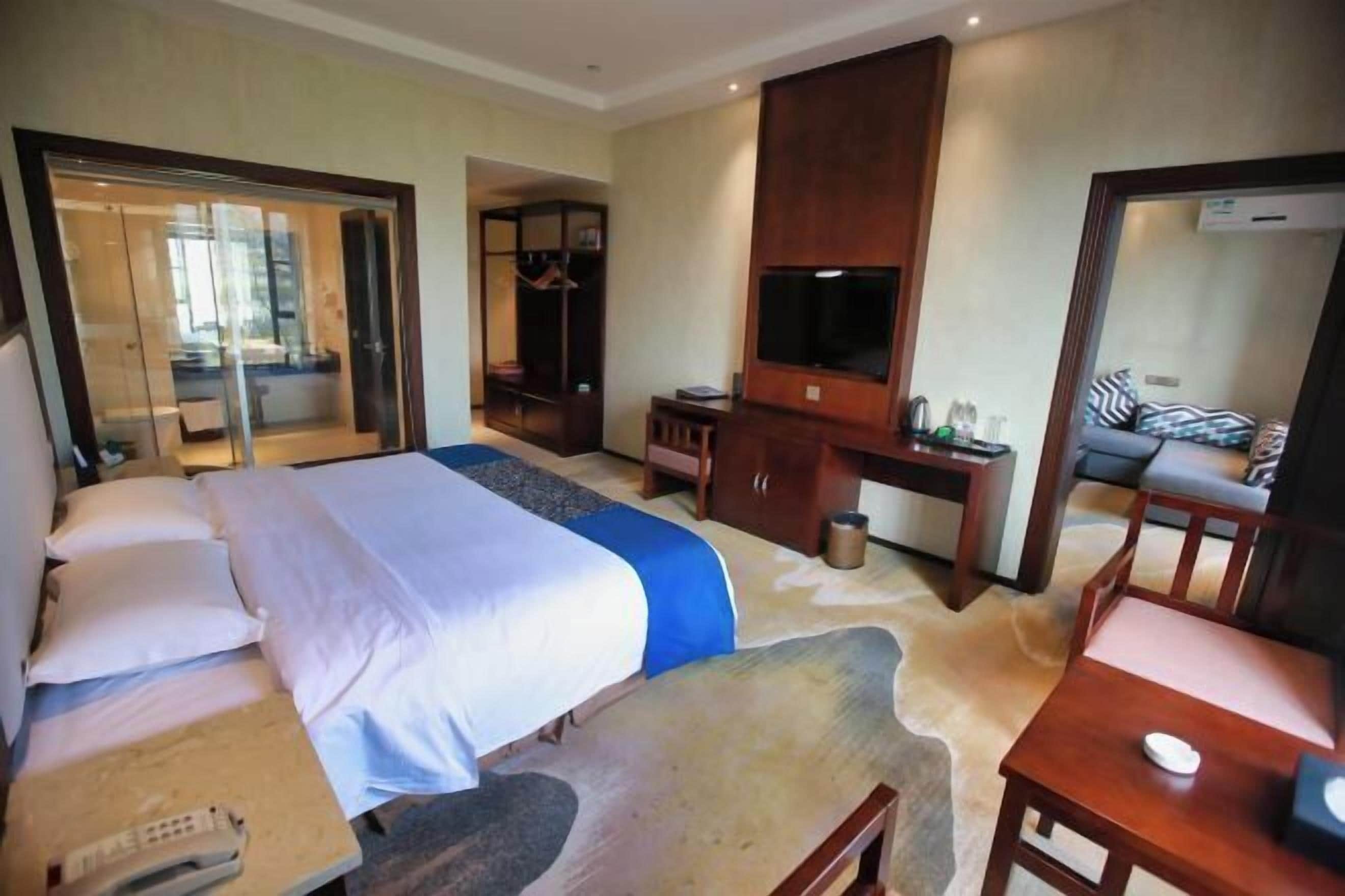 A hotel room with a bed, a desk, a chair, a TV, and a wardrobe.