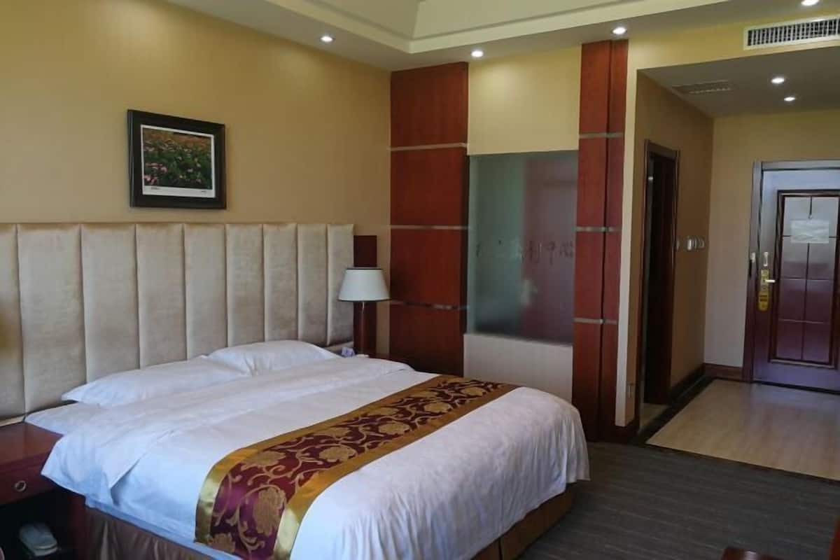 A hotel room with a large bed, a nightstand, a lamp, and a door.