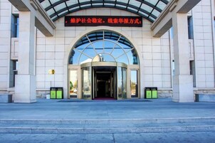 Entrada de un edificio con fachada de vidrio curvo, alfombra roja y un cartel sobre la entrada.